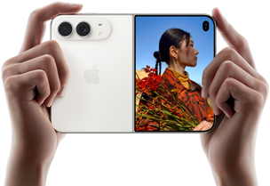 Due mani tengono un iPhone Duo bianco stellare in orizzontale, aperto; sul pannello sinistro si nota la doppia fotocamera posteriore Fusion da 48MP, mentre sul pannello destro si vede una persona che si fa fotografare sullo schermo esterno; il soggetto può vedere il proprio volto mentre viene scattata la foto grazie alla funzione Duo Preview